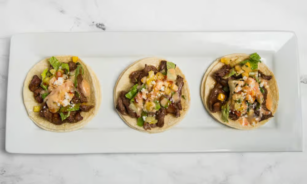 Three Hawaiian-style tacos topped with grilled meat, fresh pico, and sauce, served on a clean white background